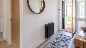 A hallway with a wooden door, a round mirror, a radiator, and a patterned rug. - Greenaway, 4 Rockhaven Gardens (Wadebridge)