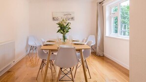 A dining room with a wooden table set for six, white chairs, a vase of flowers, and a painting on the wall. - Greenaway, 4 Rockhaven Gardens (Wadebridge)