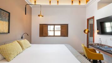 A bedroom with a large bed, a desk with a chair, a window, and a TV mounted on the wall.