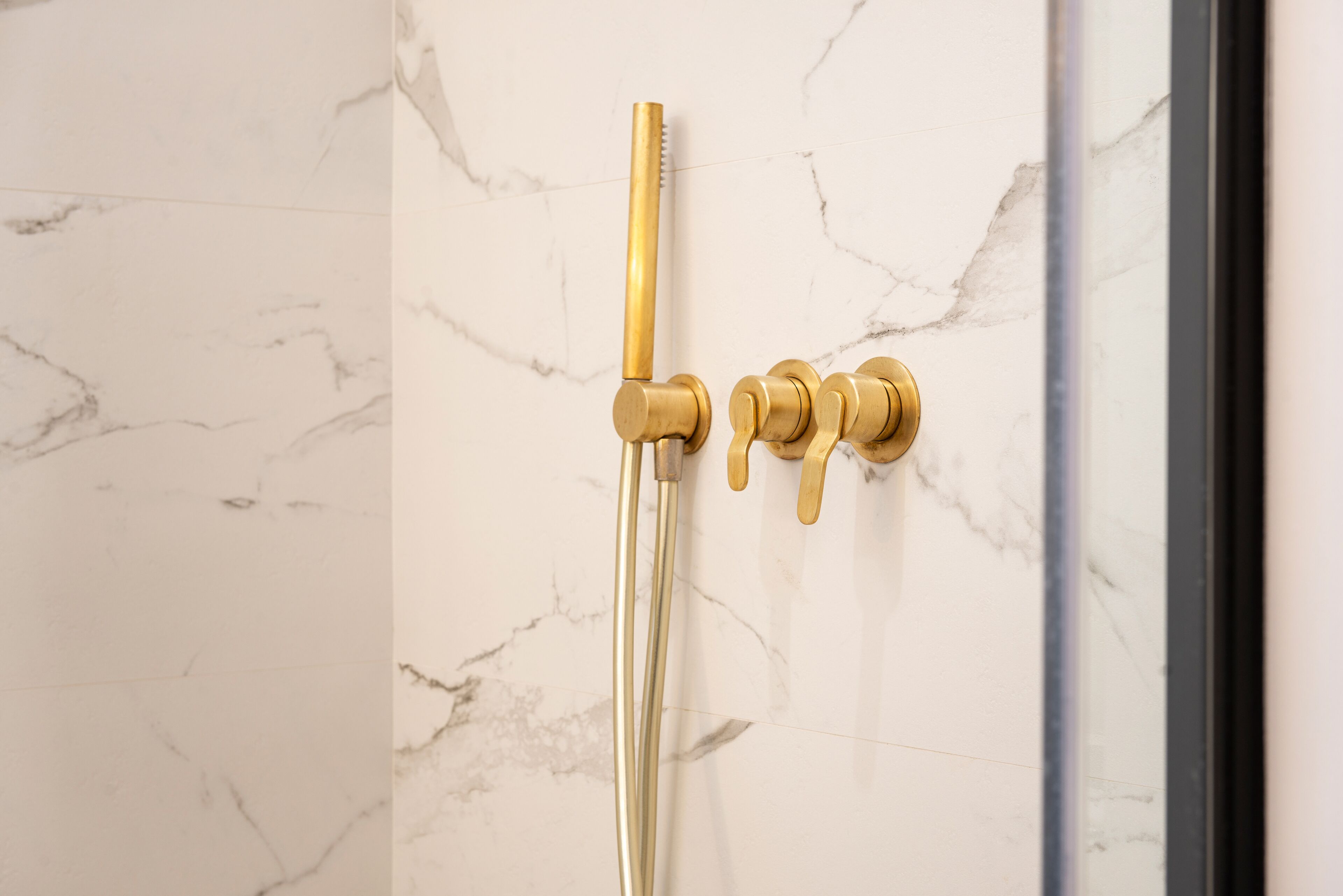 A shower with a gold faucet and controls against a marble wall.