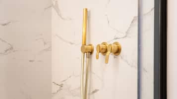 A shower with a gold faucet and controls against a marble wall.