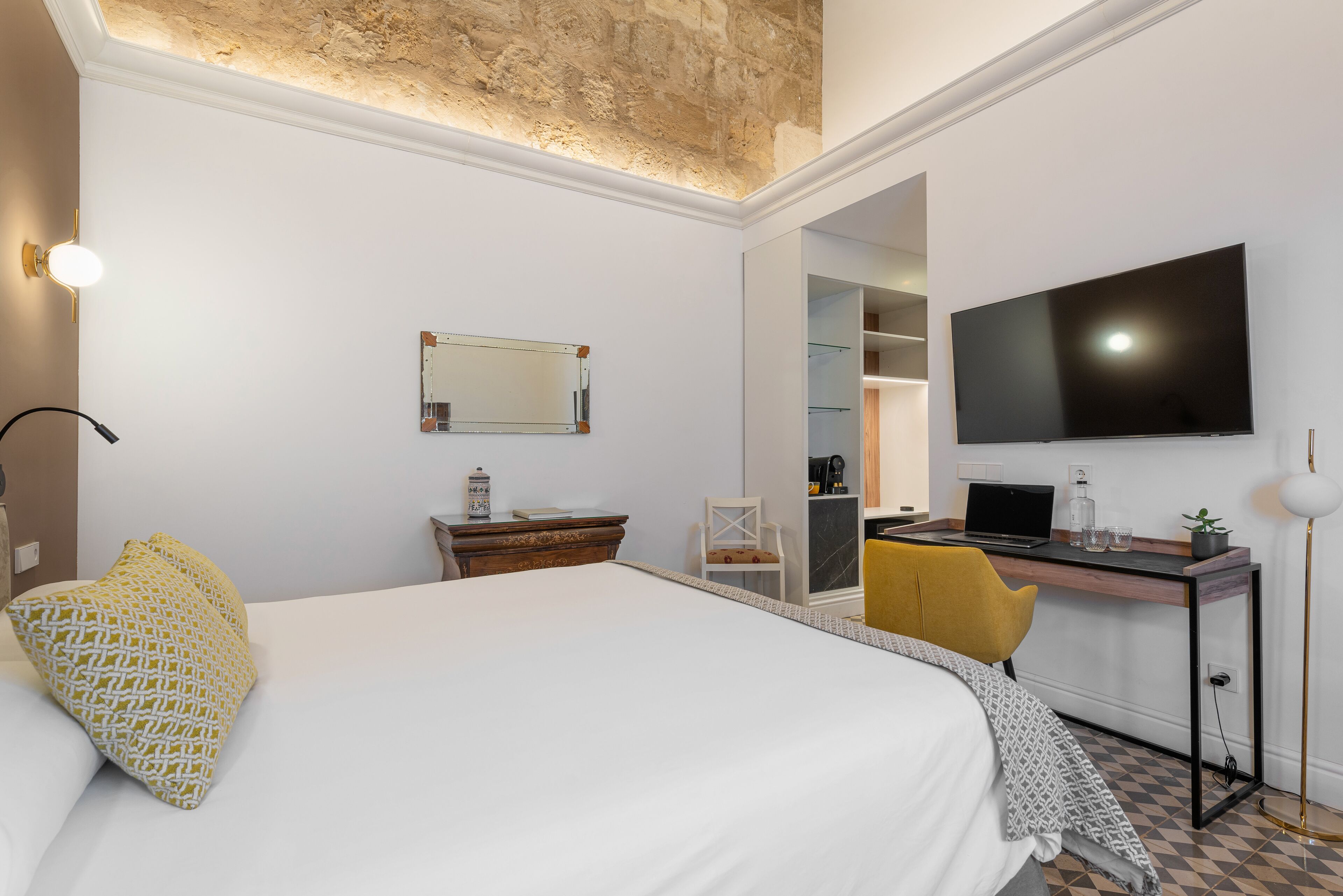 A hotel room with a large bed, a desk with a laptop, a TV, and a mirror.