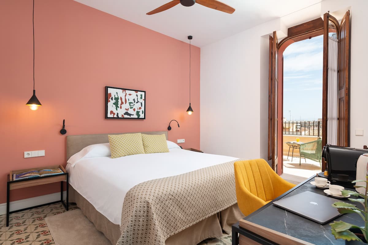 Een hotelkamer met een bed, een bureau met een laptop, een koffiezetapparaat en een balkon met uitzicht.