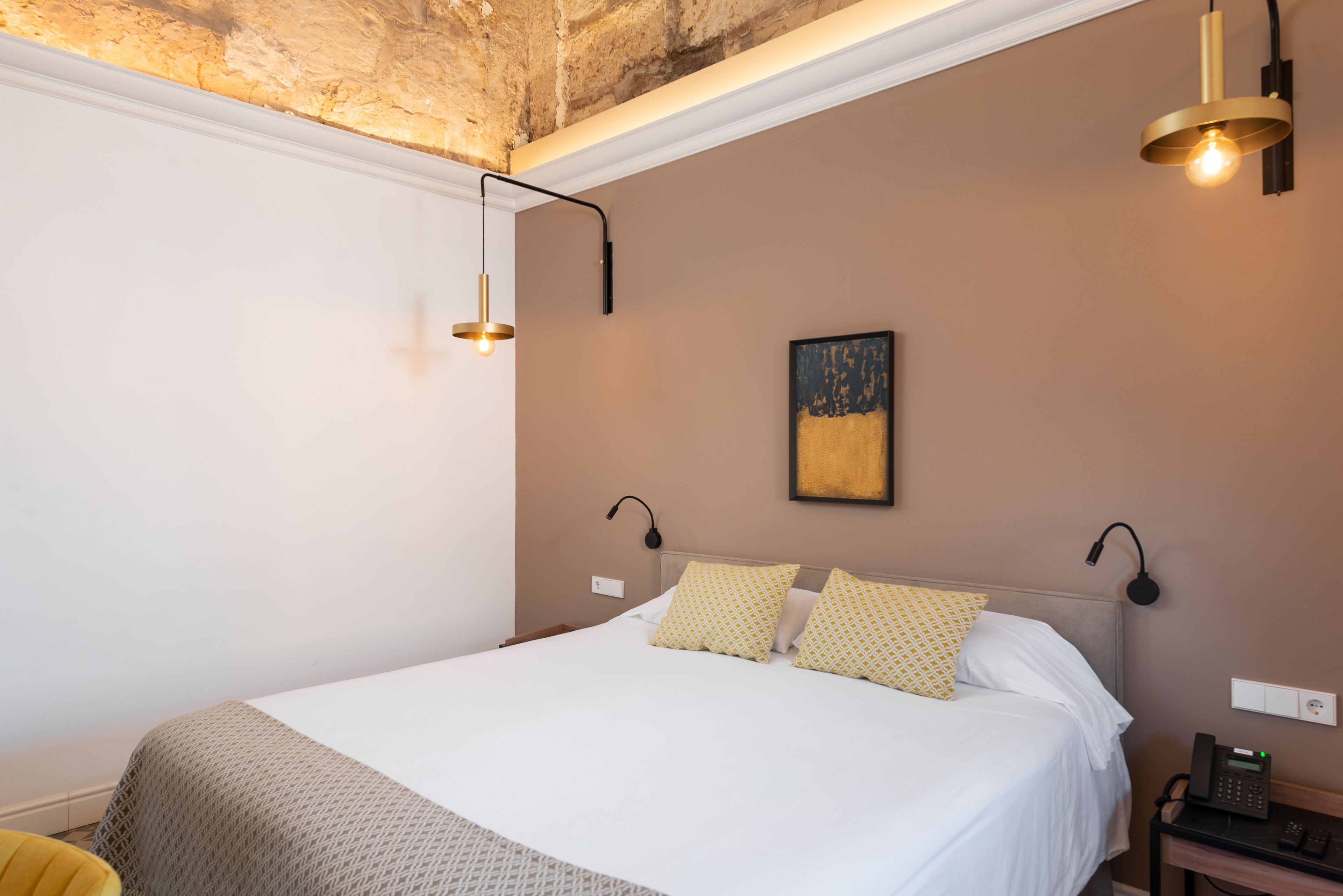 A hotel room with a large bed, two bedside lamps, a painting on the wall, and a telephone on the nightstand.