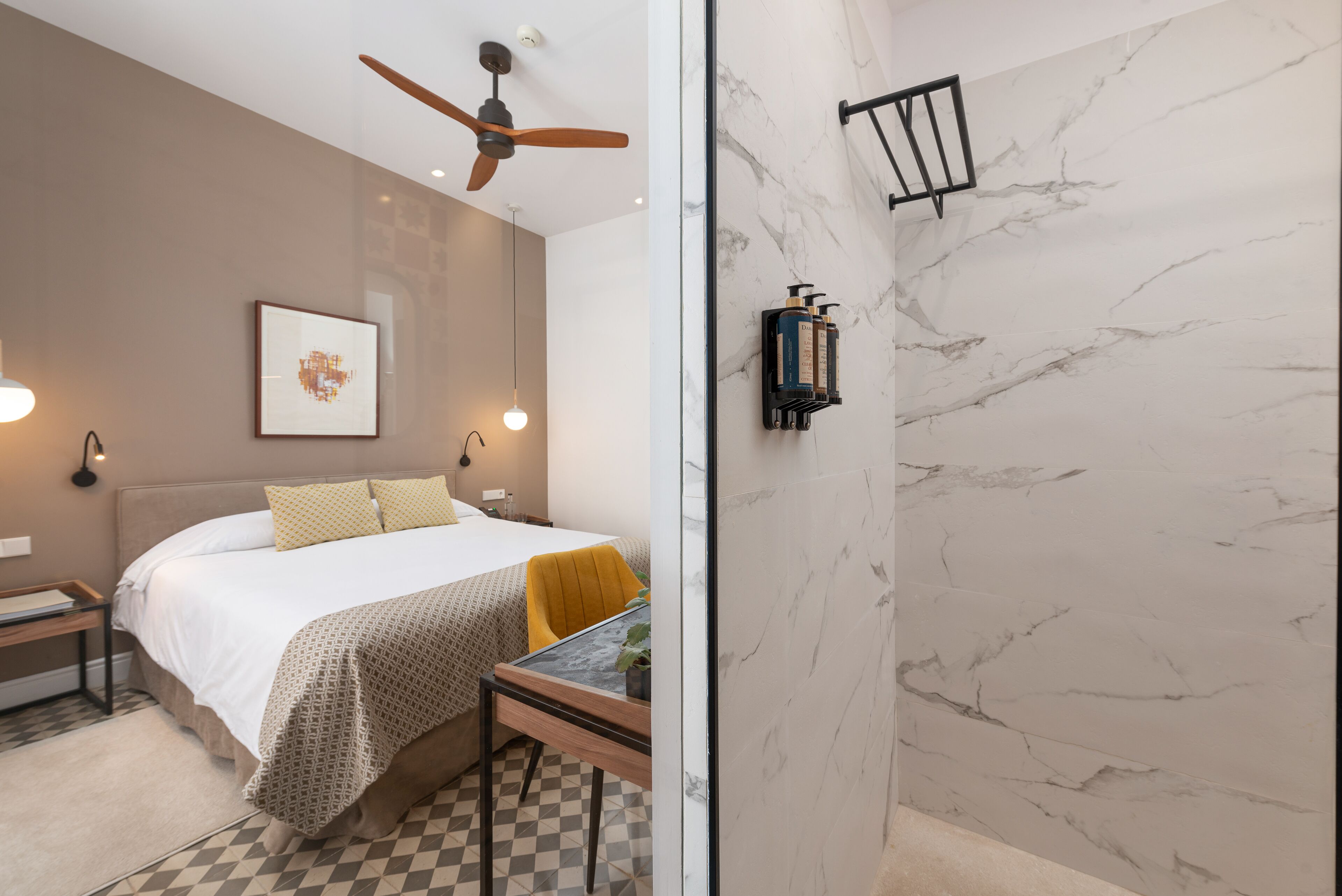 A modern hotel room with a bed, bedside table, and a small table with a chair.