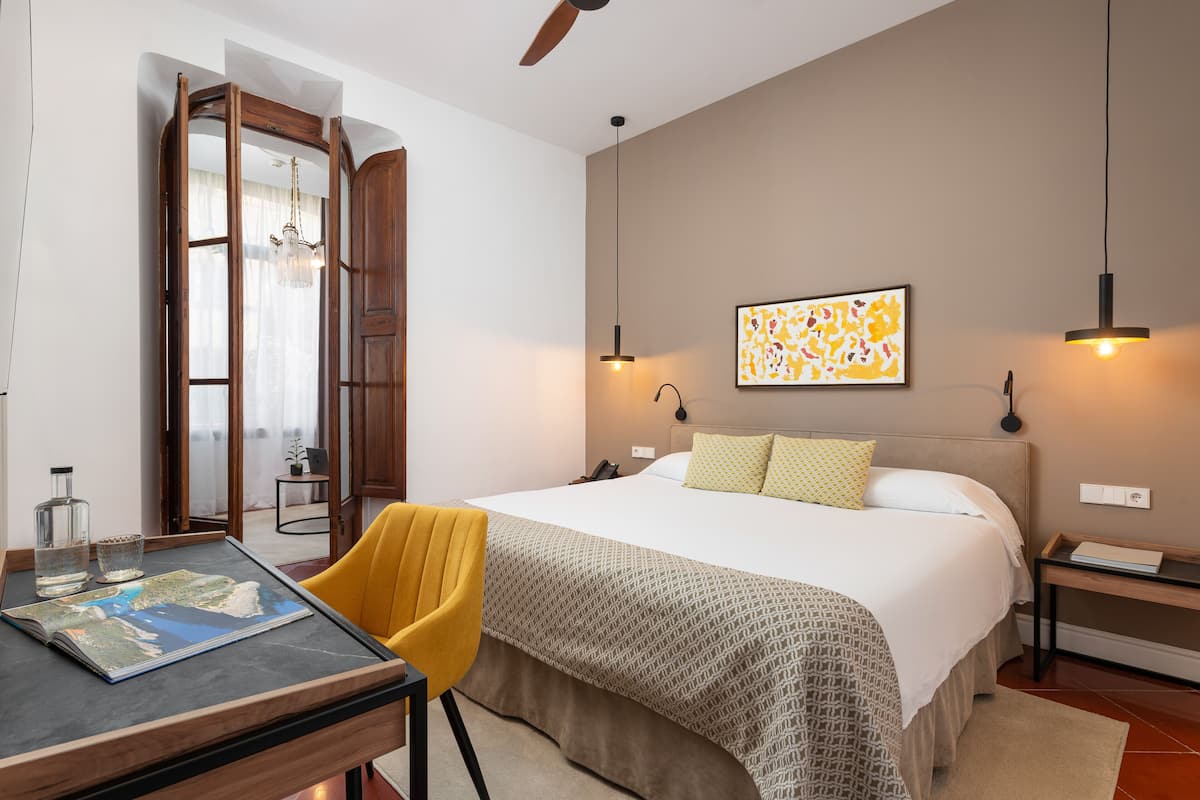 Een slaapkamer met een bed, een bureau met een kaart, een stoel, een nachtkastje en een aan de muur hangend kunstwerk.