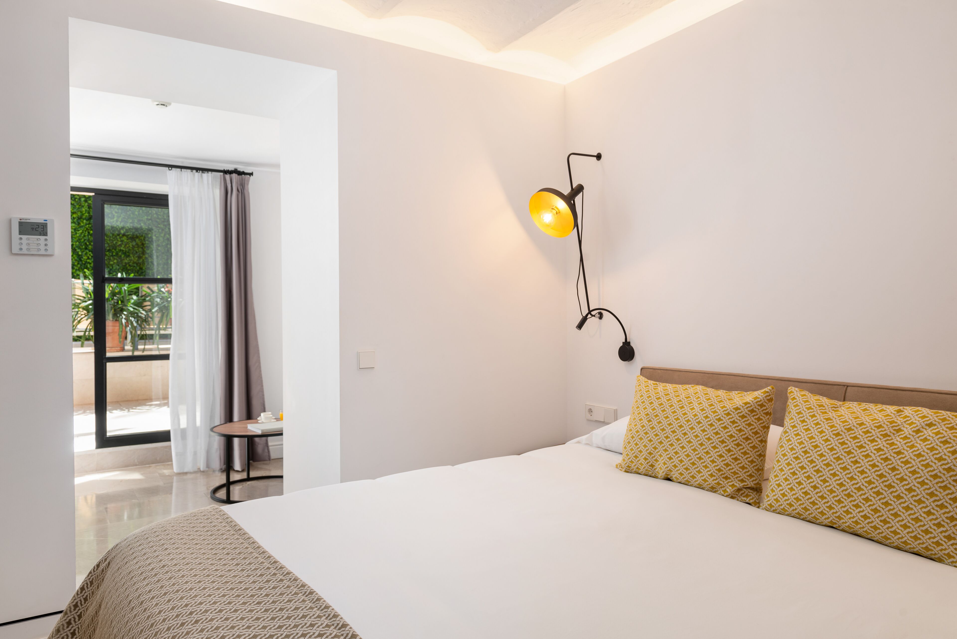 A hotel room with a large bed, a bedside lamp, and a view of a balcony with curtains.