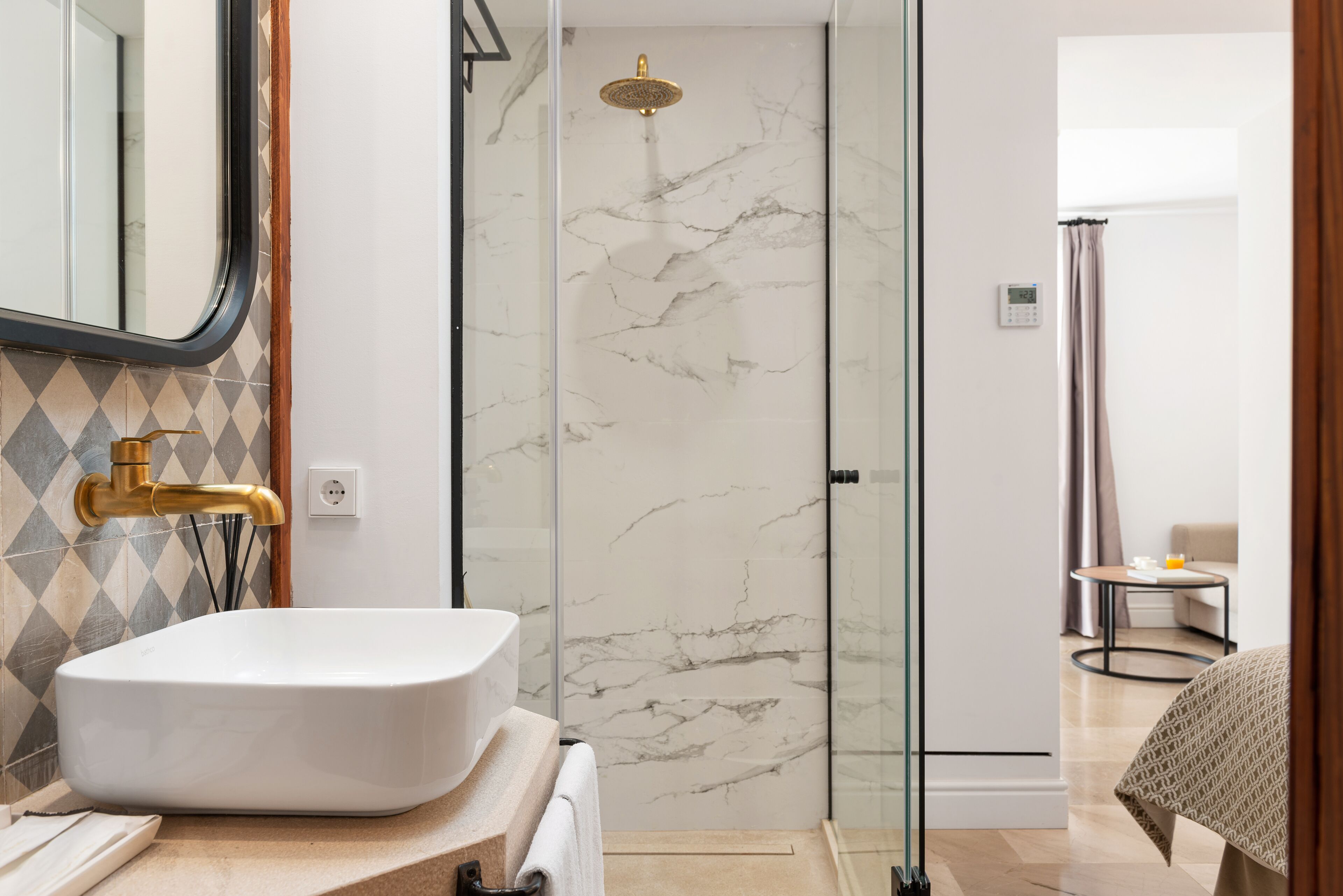 Une salle de bain moderne avec un lavabo blanc, une douche dotée d’une porte en verre et une petite table avec une chaise dans la pièce adjacente.