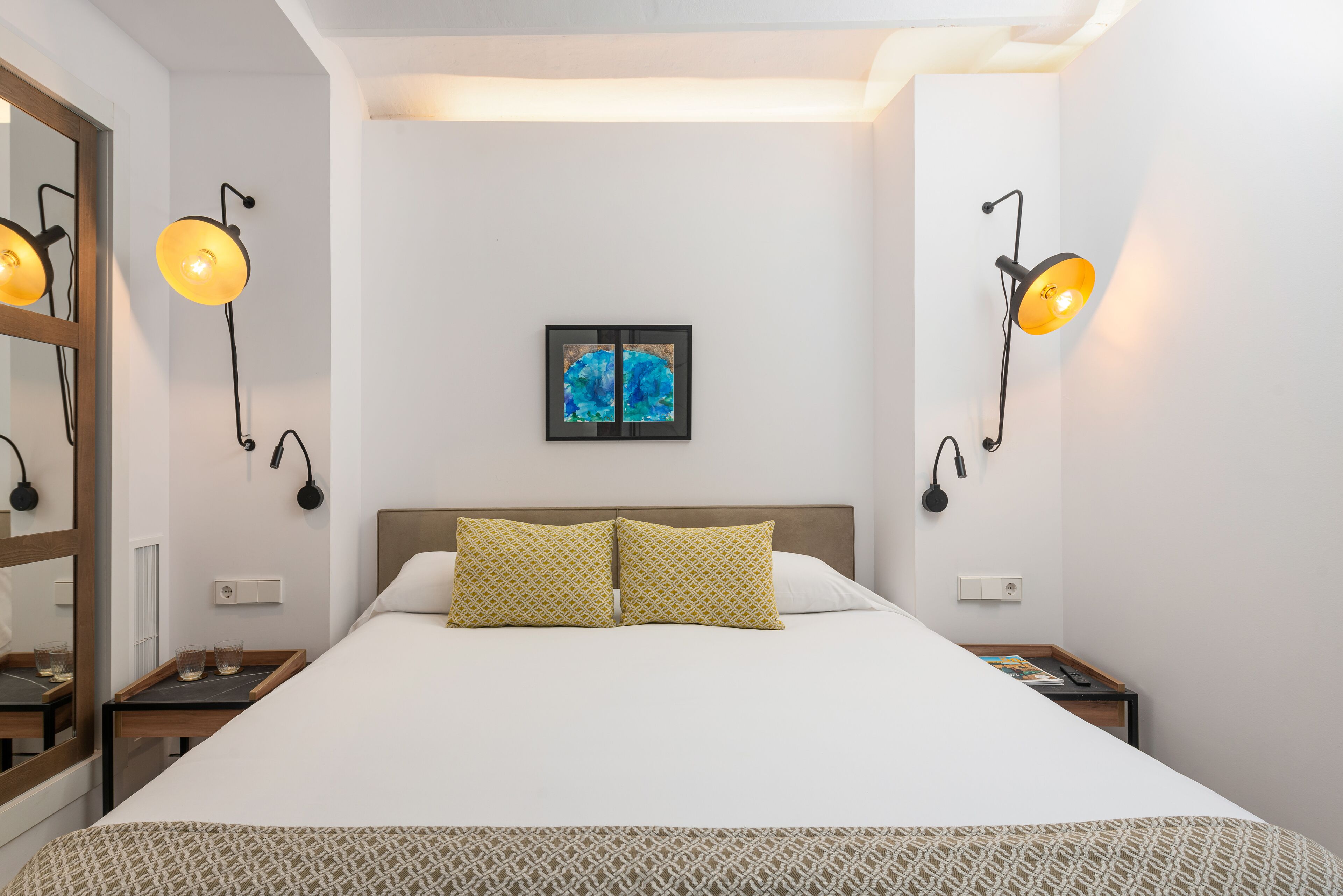 Une chambre d’hôtel bien aménagée, avec un grand lit, deux tables de chevet et des lampes fixées au mur.