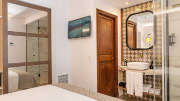 A modern bathroom with a glass shower enclosure, a wooden door, a large mirror, and a sink with a towel rack.
