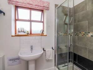 A bathroom with a sink, a window with a pink valance, a mirror, and a glass shower enclosure. - The Stables (Preston)