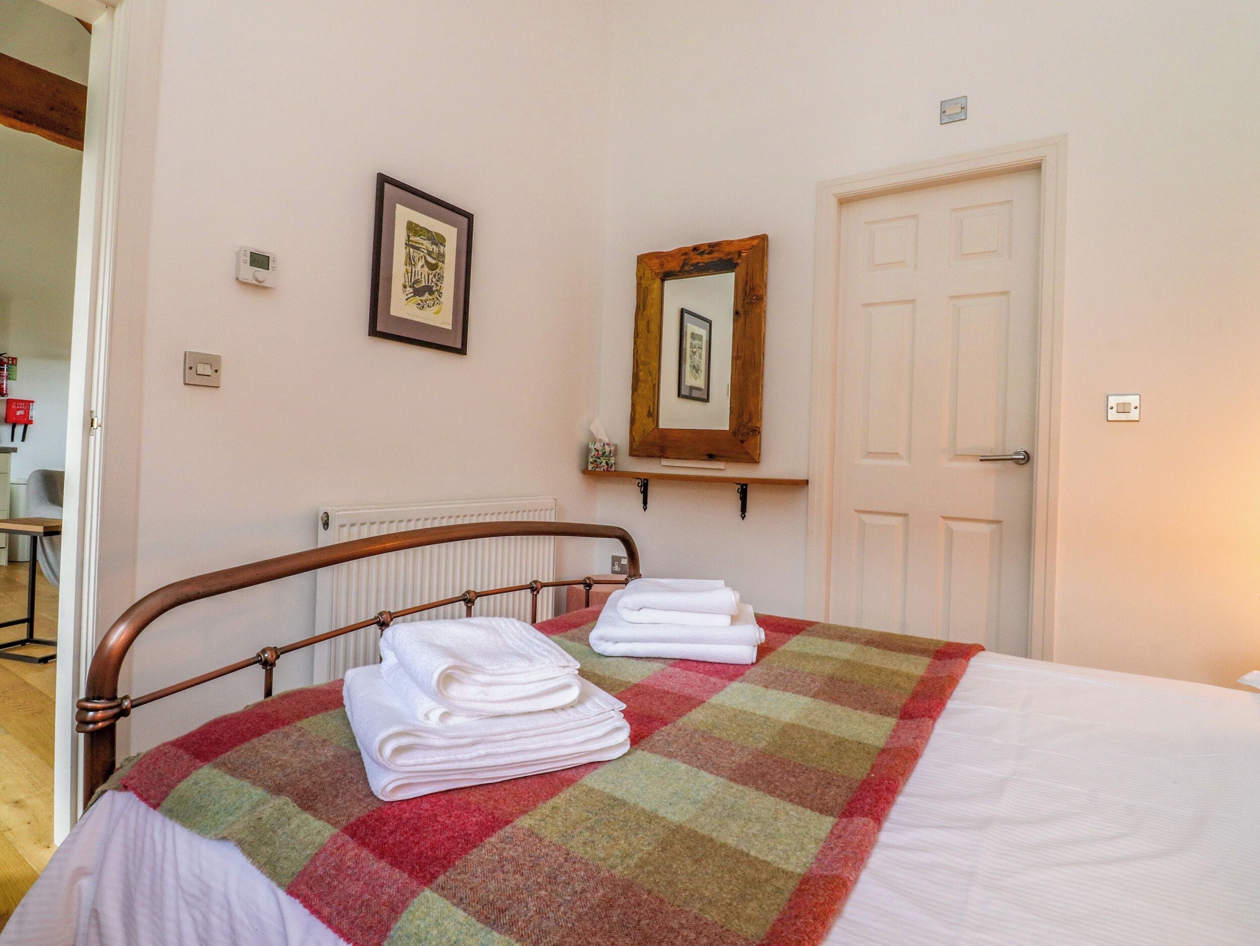 Cama bem arrumada com manta xadrez, quadro emoldurado na parede e porta com espelho.