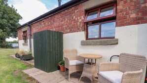 Un patio con mobiliario de mimbre y una pequeña mesa, junto a un edificio de ladrillo con un ventanal.