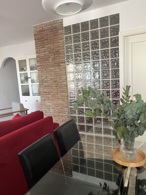 Una sala moderna con una pared de ladrillo, un separador de bloques de vidrio y un comedor con mesa y sillas.