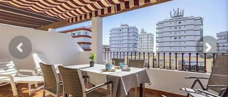 A balcony with a striped awning, a table with chairs, and a view of the San Francisco skyline.