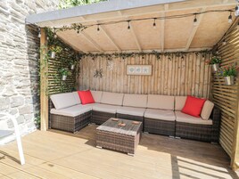 Un espacio de estar al aire libre cubierto con un sofá de mimbre, una mesa de centro y plantas colgantes.