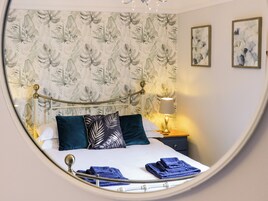 Un dormitorio con cama, almohadas, una mesita de noche, una lámpara y un papel tapiz floral.