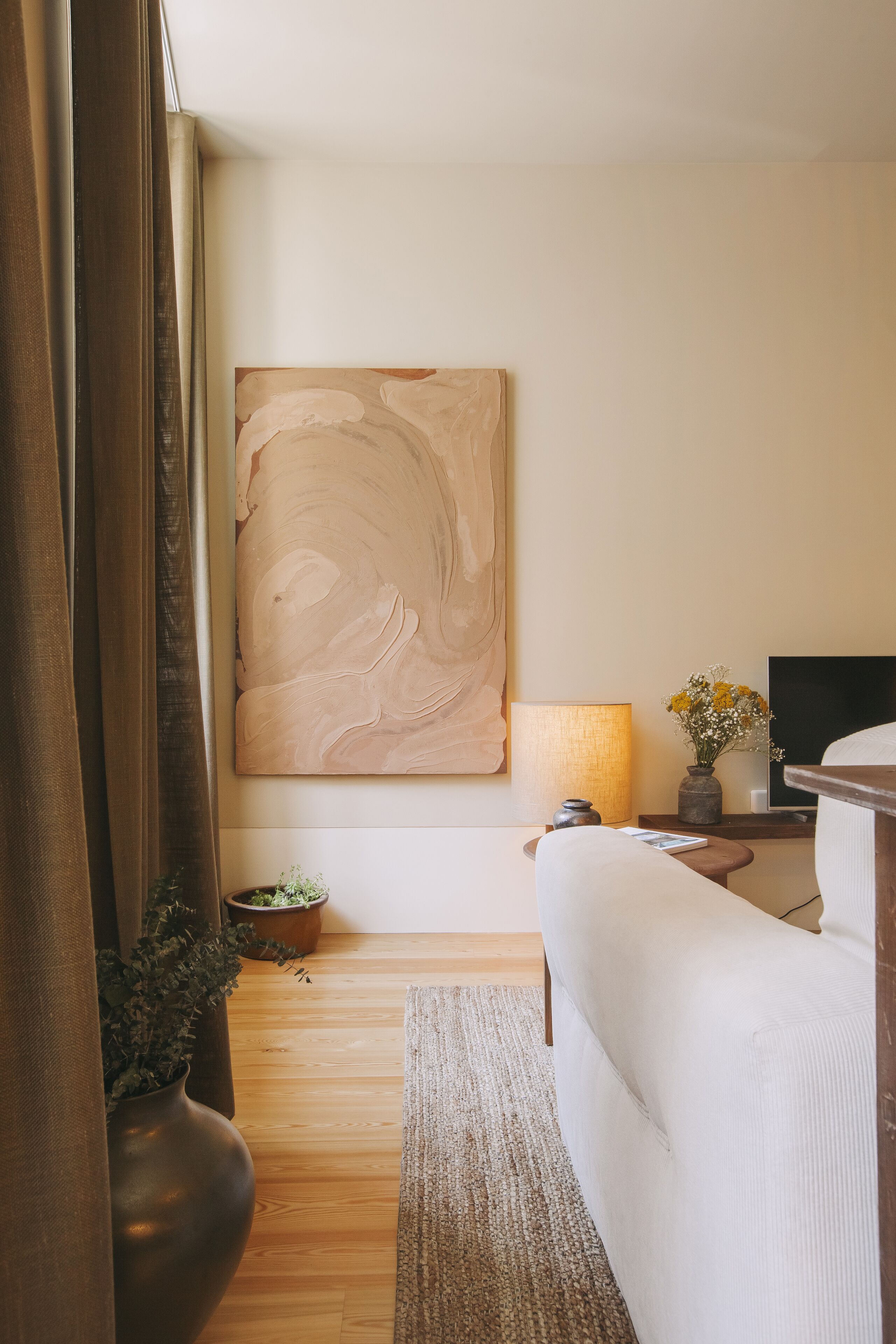 A modern living room with a large abstract painting, a sofa, a TV, a lamp, and a small table with a vase of flowers.