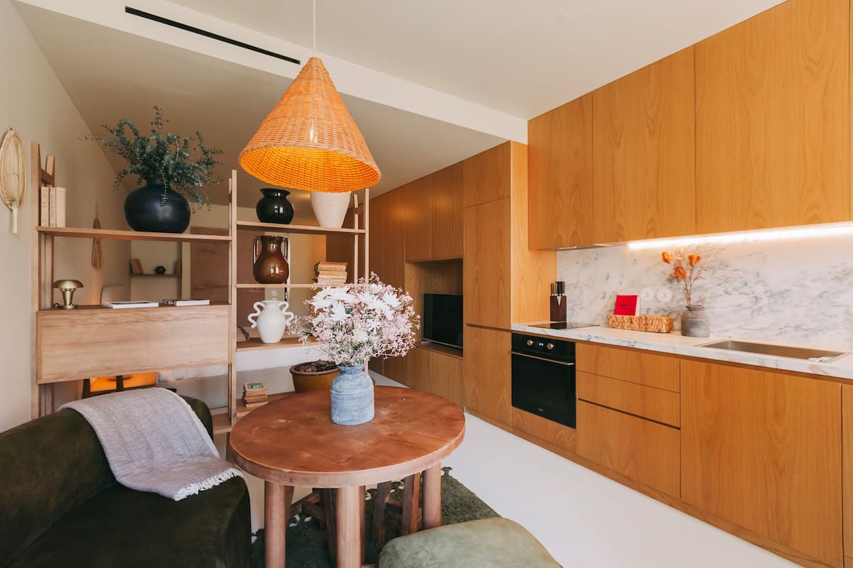 A modern kitchen with wooden cabinets, a round wooden table, and a hanging orange lamp.