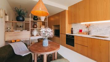 Une cuisine moderne avec des meubles de rangement en bois, une table ronde en bois et une lampe orange suspendue.