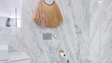Un baño moderno con inodoro blanco, cabina de ducha de vidrio y salpicadero de mármol.