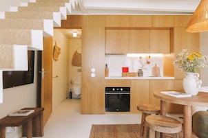 Una cocina moderna con armarios de madera, horno empotrado y una zona de comedor con taburetes.