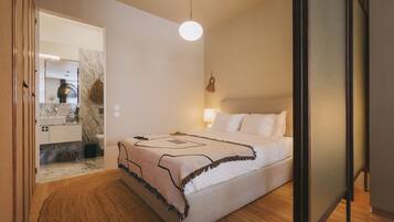 Un dormitorio moderno con una cama grande, una mesita de noche, una lámpara y vistas a un baño con encimera de mármol.