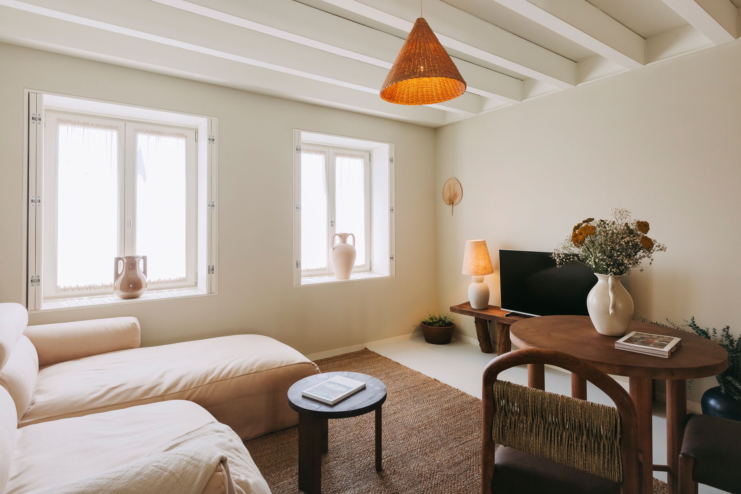 A cozy room with two beds, a TV, a table with a vase, and a window with a view.