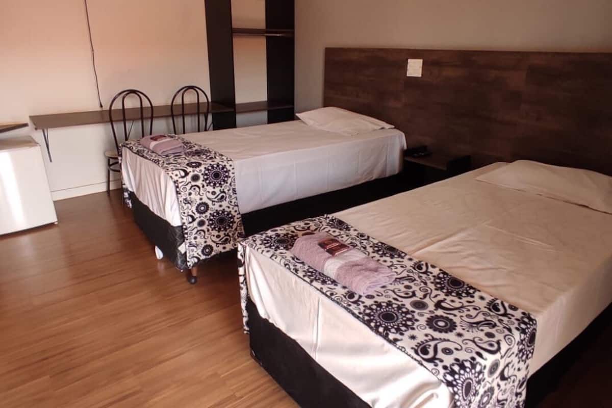 Quarto de hotel com duas camas, uma kitchenette pequena e uma TV fixada na parede.