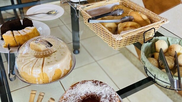A buffet setup with various food items including a cake, bread, and a fruit bowl. - Hotel nova barrinha (Barrinha)