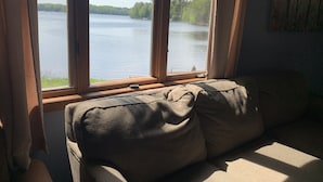 Una habitación con un ventanal grande con vistas a un lago, marco de madera y un sofá color beige.