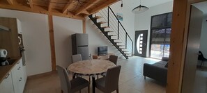 Eine moderne Küche mit Holzboden, einem Essbereich mit rundem Tisch und Stühlen, einem integrierten Fernseher und einer Treppe, die zu einem Balkon führt.
