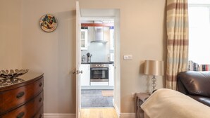 Una habitación con un aparador de madera, una cama, una lámpara y vistas a una cocina con armarios blancos y una estufa.