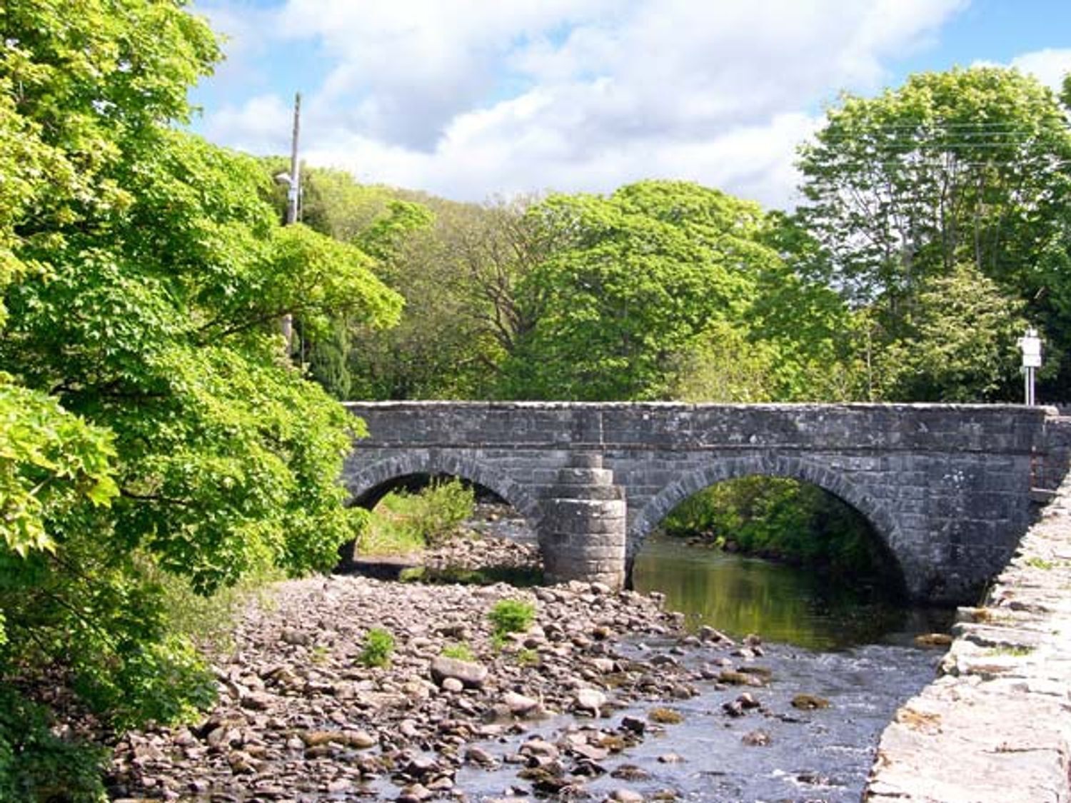 Eine Steinbrücke über einem Fluss, umgeben von viel Grün.