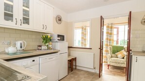 A kitchen with white cabinets, a microwave, a kettle, and a dining area with a chair and table. - Dove's Nest (Great Yarmouth)