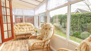 A sunlit room with a large window, wicker furniture, and a view of a garden. - Dove's Nest (Great Yarmouth)