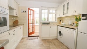 A modern kitchen with white cabinets, a built-in oven, a washing machine, and a coffee maker. - Dove's Nest (Great Yarmouth)
