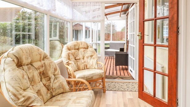 A sunroom with wicker chairs, large windows, and a view of the backyard. - Dove's Nest (Great Yarmouth)