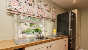 Una cocina con un refrigerador de acero inoxidable, un lavamanos con grifo y una ventana con cortina estampada.