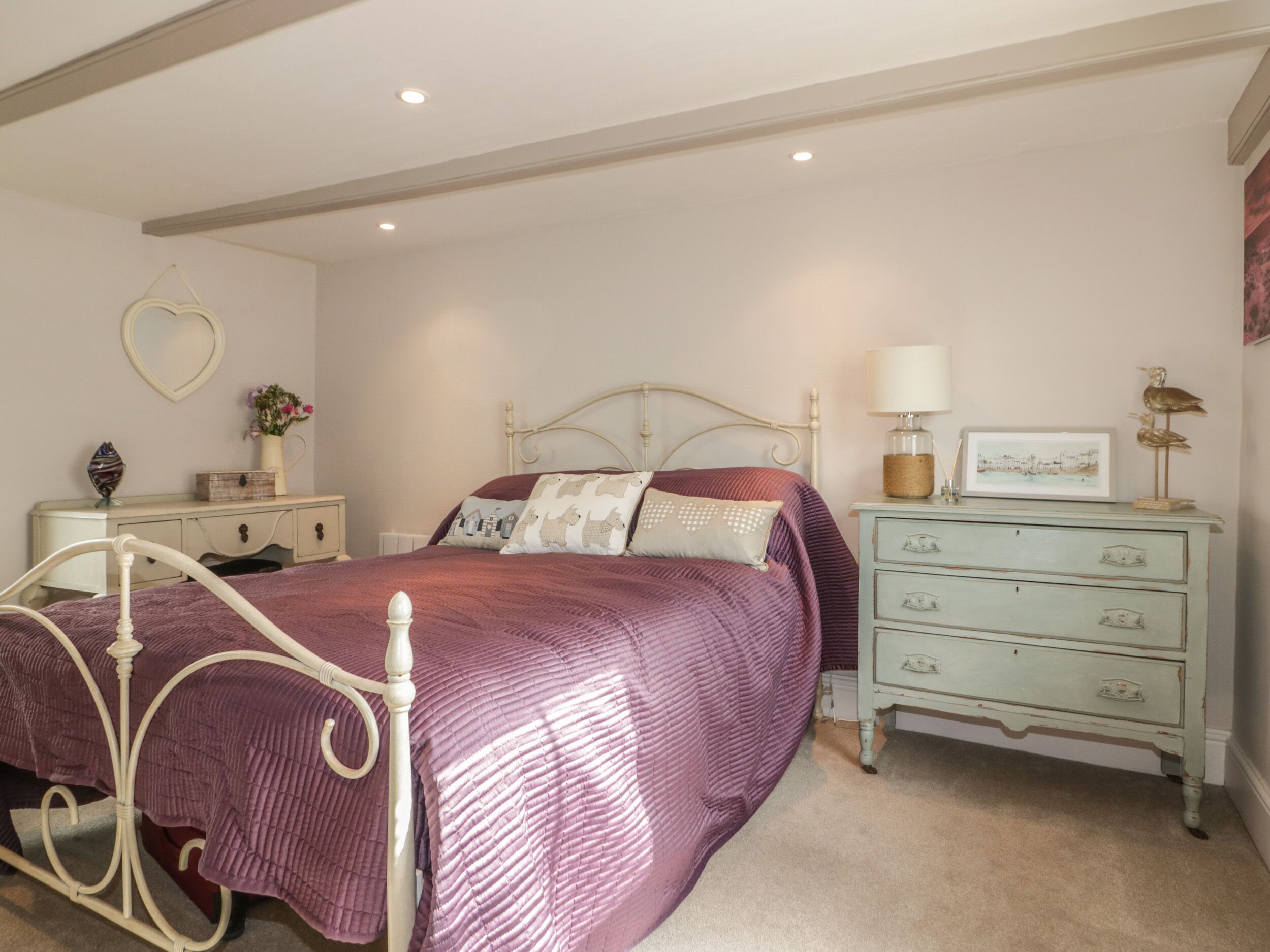 Une chambre à coucher avec un lit, une commode, une table de chevet et un miroir en forme de cœur accroché au mur.