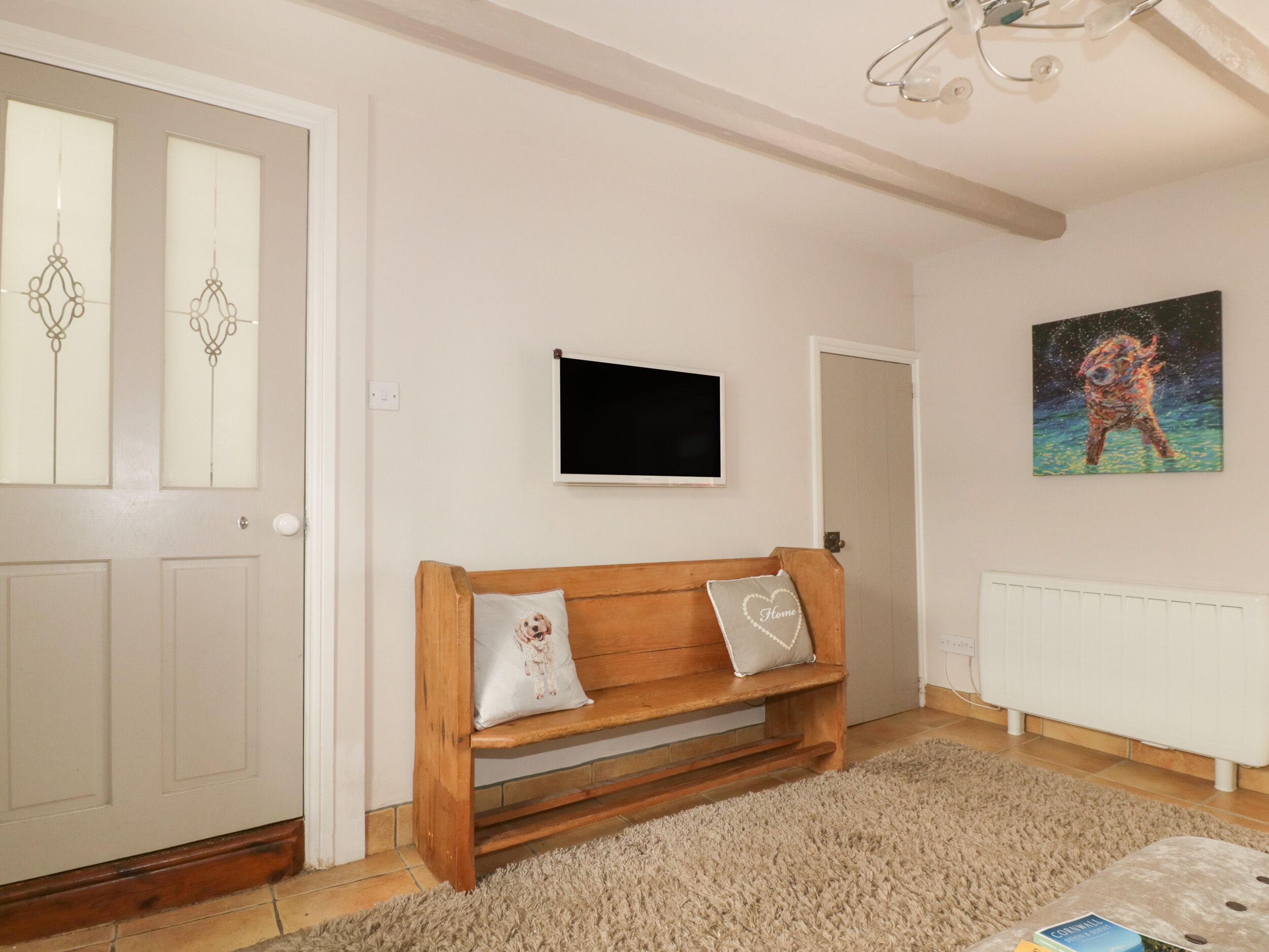 Una habitación con un banco de madera, un televisor fijado a la pared, un cuadro y un radiador.
