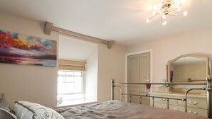 A bedroom with a bed, a dresser, a mirror, and a painting on the wall. - Blue Crab Cottage (St Austell)