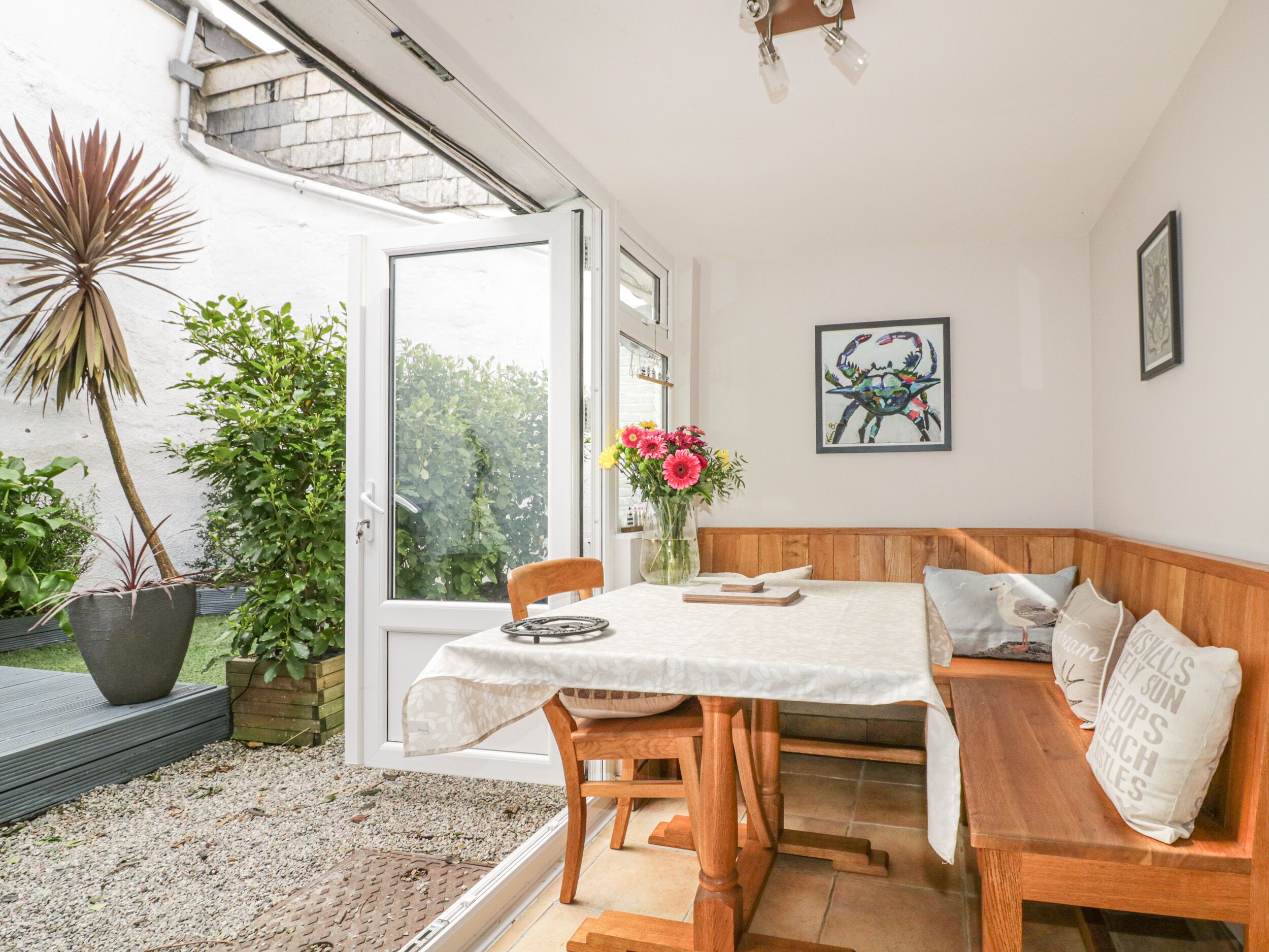 A dining area with a wooden bench, a table with a white tablecloth, and a vase with flowers.