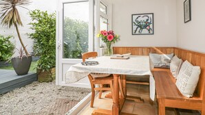 A dining area with a wooden bench, a table with a white tablecloth, and a vase with flowers. - Blue Crab Cottage (St Austell)