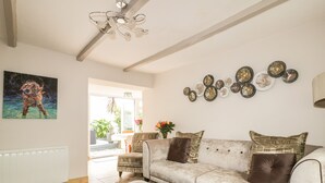 A living room with a sofa, ottoman, and a painting of a dog. - Blue Crab Cottage (St Austell)