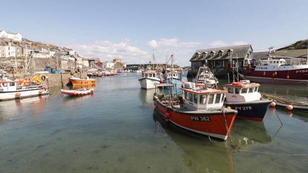 A harbor with multiple boats docked, clear water, and buildings in the background. - Blue Crab Cottage (St Austell)