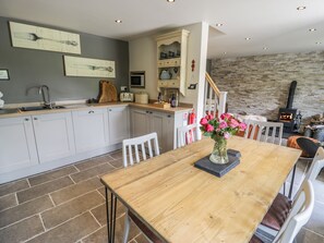 A modern kitchen with grey cabinets, a wooden dining table, and a stone wall. - Swn yr Afon (Caernarfon)