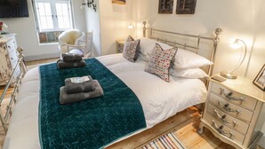 Een slaapkamer met een bed, nachtkastjes, een stoel, een raam en een kunstwerk aan de muur.