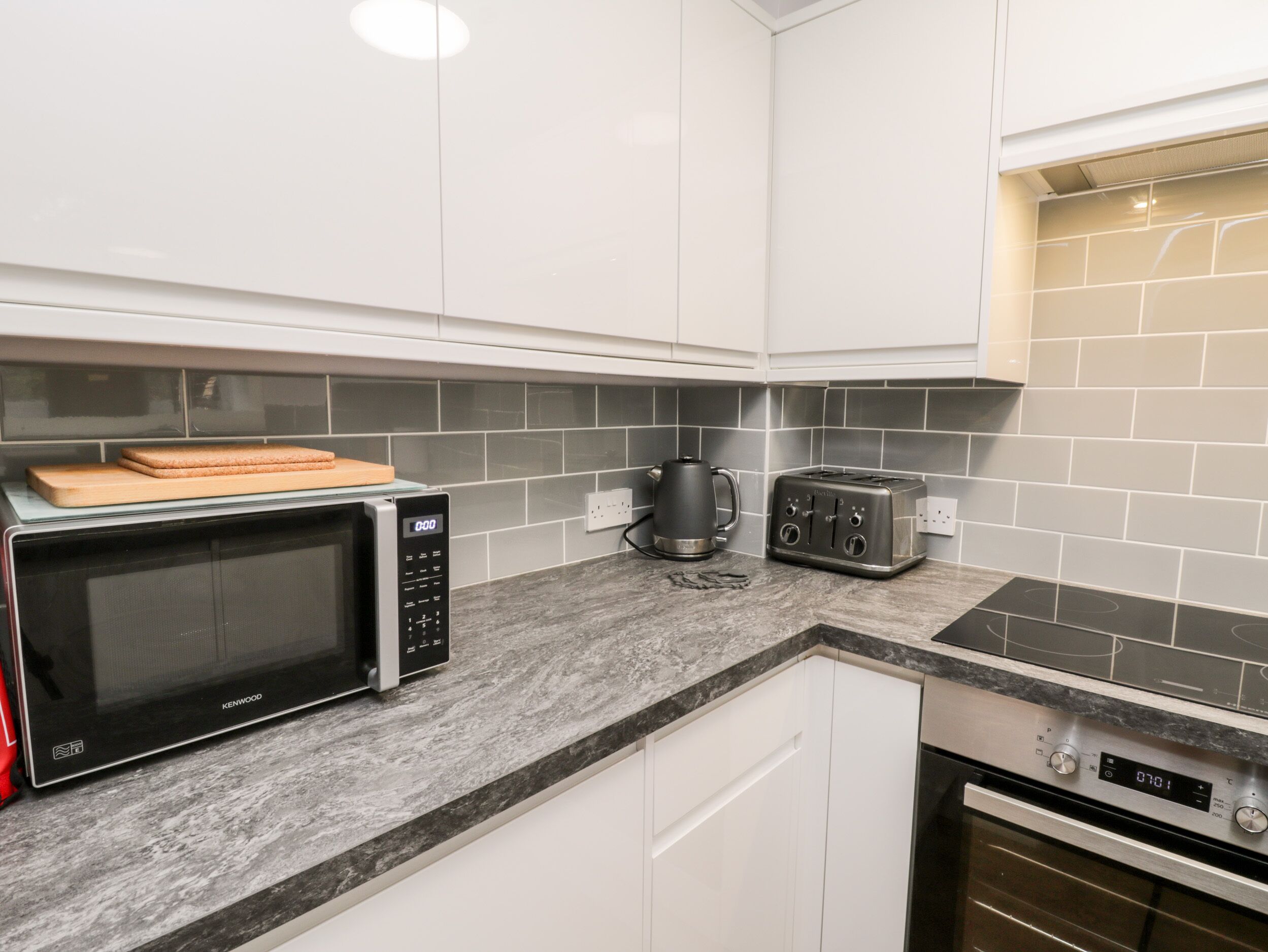 A modern kitchen with white cabinets, a black microwave, a toaster, and a kettle on the countertop.