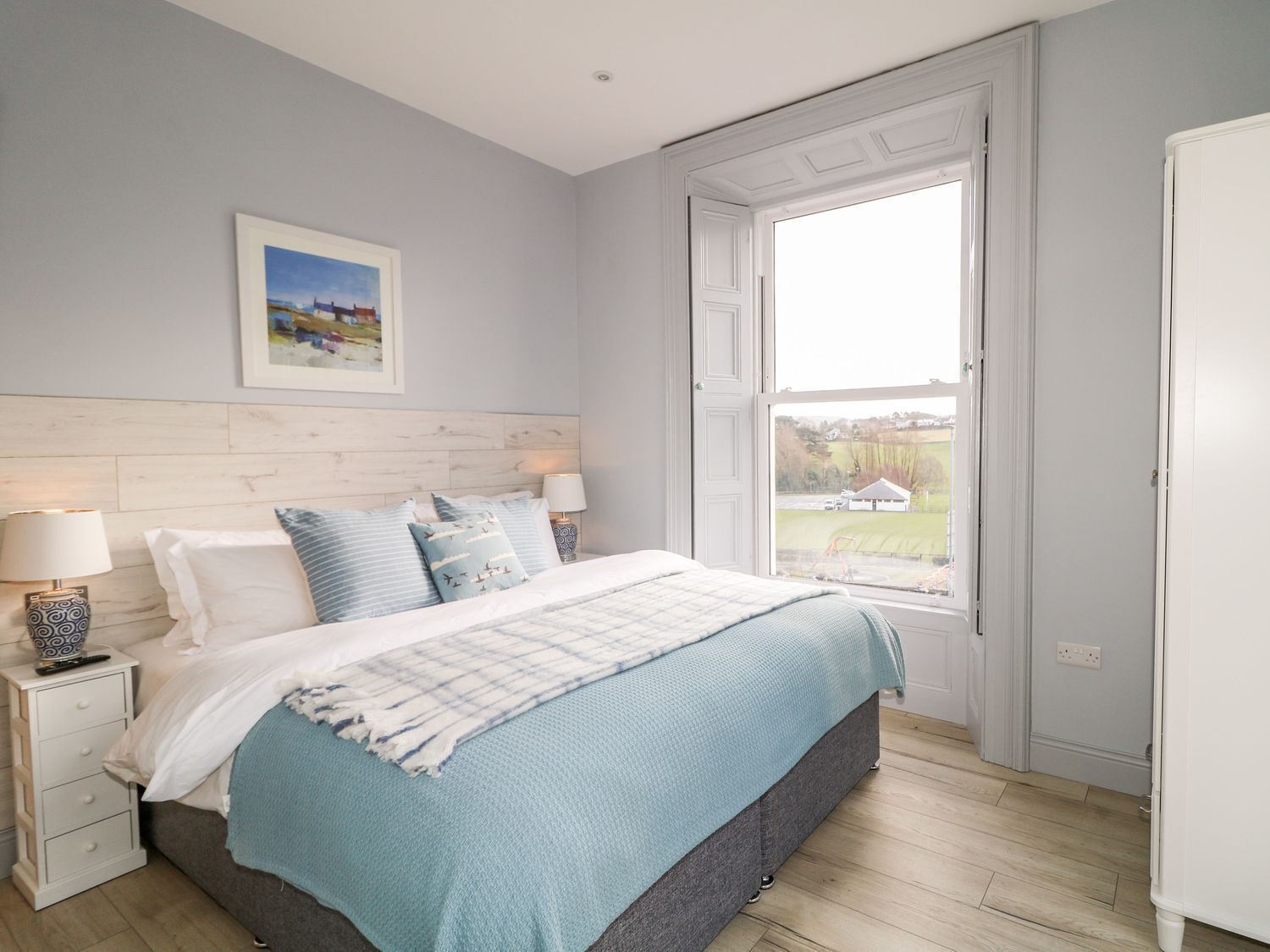 A bedroom with a bed, two bedside tables, a window with a view, and a door.